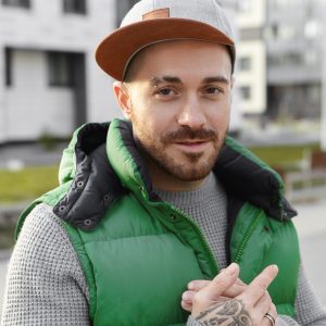 People, modern lifestyle, urban style and street fashion concept. Confident stylish unshaven young guy with pierced eyebrow and tattoo on his hand having great plan, walking outdoors on city streets